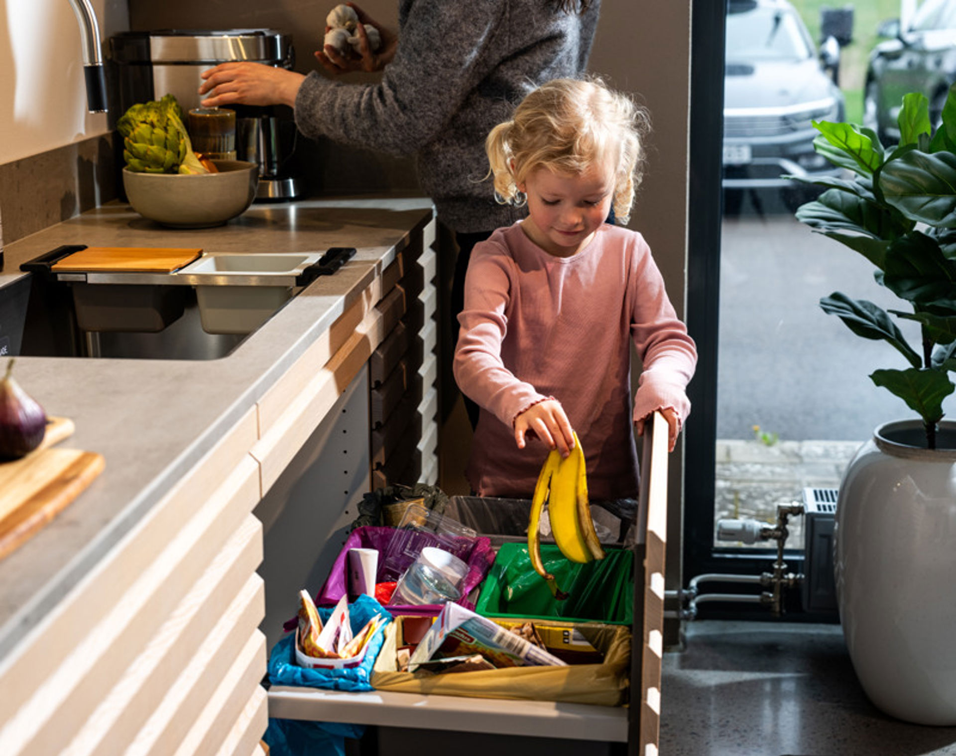 En kvinna och en liten flicka i ett kök som färgsorterar sina sopor. 